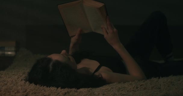 Молодая Женщина Читает Книгу Тускло Освещенной Комнате Лежит Спине — стоковое видео