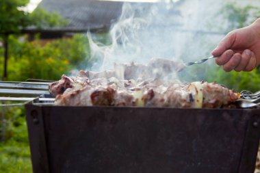 Caddedeki ızgarada şiş kebap. Tüttür. Elinde şiş var.