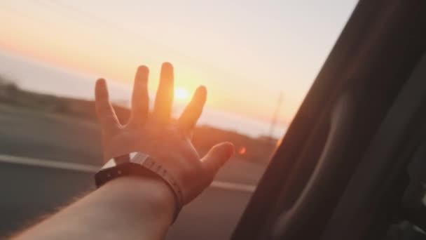 Ręka Mansa sięga po słońce przez okno samochodu, zwolnione tempo. Ostatnie promienie zachodzącego słońca — Wideo stockowe