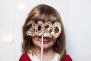 Noel Baba gibi giyinmiş güzel mutlu küçük bir kızın portresi, 2020 numaralar taşıyor, beyaz arka planda izole edilmiş. Noel ve Yeni Yıl. Noel Baba partisi. Tatil kutlamaları. Seçmeli odaklanma.