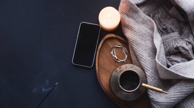Kış konsepti. Gri örgü süveter, mum, kahve içeceği, günlük, telefon, siyah masadaki bardaklar. Soğuk havada sıcak bir hafta sonu. karanlık atmosfer