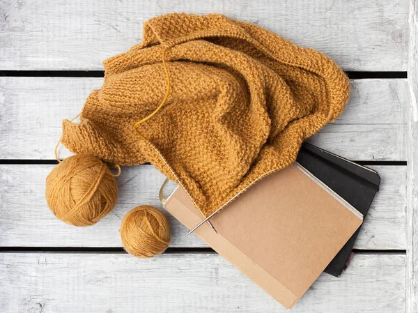 Women\'s hobby. Crochet and knitting. Working space.  diary , balls of mustard yarn, needles, knitwear, crochet hooks on the wood table.flat lay/copy space.autumn, cozy,freelance concept