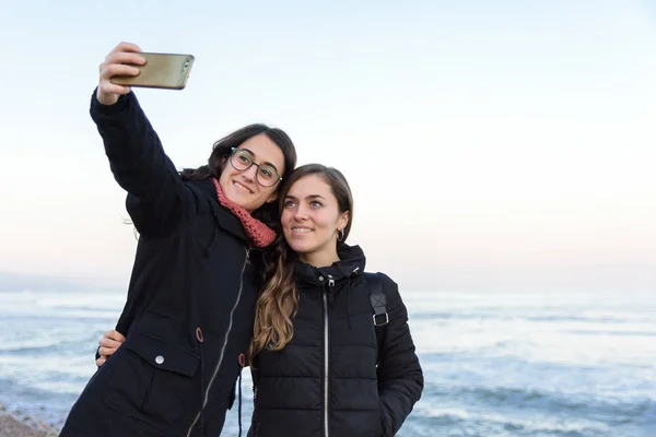 Dwa młody kaukaski dziewczyna co a selfie razem na plaża w zimie — Zdjęcie stockowe