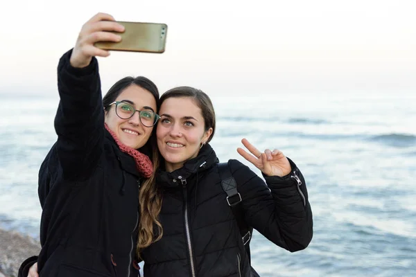 Dwa młody kaukaski dziewczyna co a selfie razem na plaża w zimie — Zdjęcie stockowe
