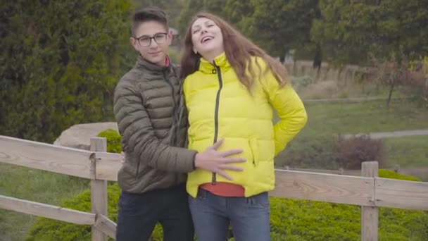 年轻的白人男孩 戴着眼镜 爱抚着他穿着黄色外套微笑的怀孕母亲的腹部 快乐的母亲和她的成年儿子在户外共度秋日 良好的关系 — 图库视频影像