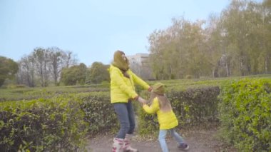 Açık havada oynayan sarı ceketli mutlu bir beyaz aile. Kızı, sonbahar parkında annesinin etrafında dönüyordu. Neşeli anne çocuğuyla dinleniyor.