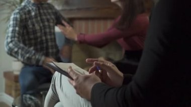 Beyaz erkeklerin ellerinde evrak ve kalemle yakın çekim. Arka planda duygusal olarak kavga eden genç bir aile. Psikolog sabırla müvekkillerinin sakinleşmesini bekliyor. Çift terapisi..