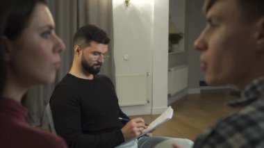 Sakallı psikolog gibi konuşan beyaz bir kadın ve erkeğin yakın plan fotoğrafları. Arka plandan onlara bakıyor. Çift terapisi seansında profesyonel psikolog. Aile sorunları.