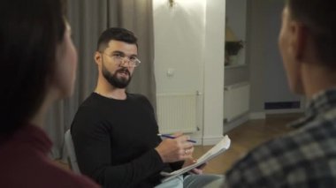 Zarif gözlüklü yakışıklı beyaz psikolog hastalarıyla konuşuyor ve notlar alıyor. Kadın ve erkek sorunlarını çözmeye çalışıyor. Profesyonel psikolog ve çift terapisi..