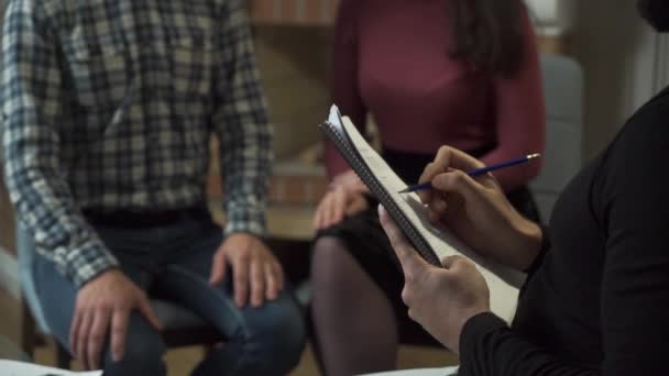 Mains blanches masculines prenant des notes et gestualisant au premier plan. Jeune couple caucasien ou famille tenant la main à l'arrière-plan. Homme et femme reçoivent des nouvelles au bureau des psychologues .
