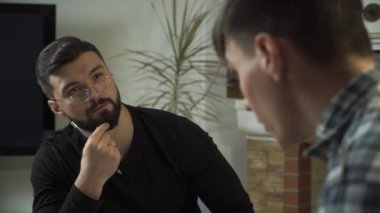 Gözlüklü beyaz erkek psikoloğun hastasını dinlediği yakın plan. Genç adam ilk kez psikolojik muayenehaneye geldi. Bireysel terapi, sorunları çözme.