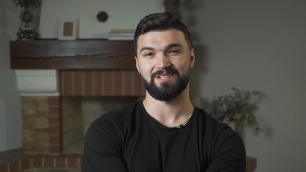 Retrato de close-up de belo homem caucasiano com cabelo preto e barba falando na câmera. Cara atraente sentado em casa . — Vídeo de Stock