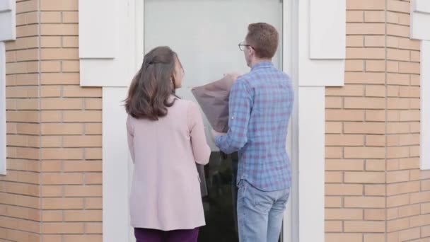 Baksidan av unga vita par kommer till entrén dörren med en bukett röda rosor och tårta. Nervös rödhårig man i glasögon får panik innan han träffar sina flickvänner föräldrar. — Stockvideo