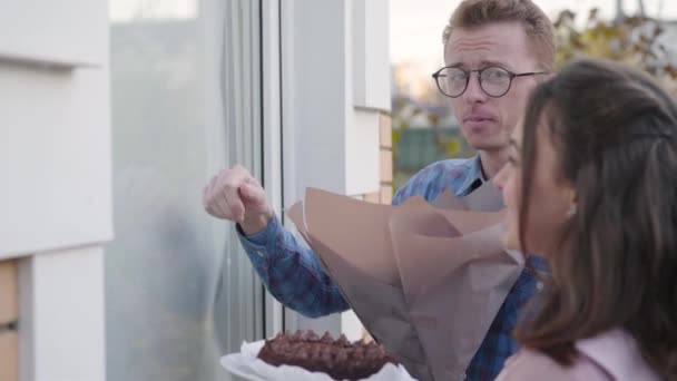 Side view of nervous redhead Caucasian man in eyeglasses knocking the door. His fiancee standing next to him with a delicious cake. Meeting with parents, acquaintance, family gathering. — Stock Video