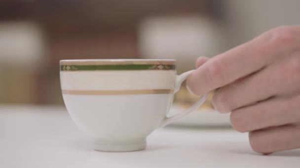 Primer plano de la taza blanca con té o café de pie en la mesa. Hombre adulto caucásico mano tomándolo y poniendo de nuevo en pocos momentos . — Vídeos de Stock