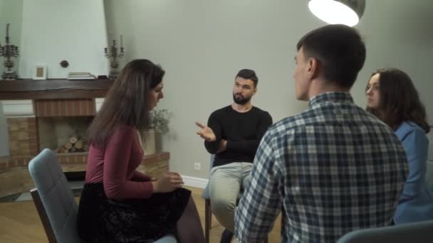 Vier kaukasische Menschen sitzen auf Stühlen im Kreis und unterhalten sich. junge schöne Frau, die mit Freunden über ihre Probleme spricht. Gruppentherapie, psychologische Behandlung, Empathie. — Stockvideo