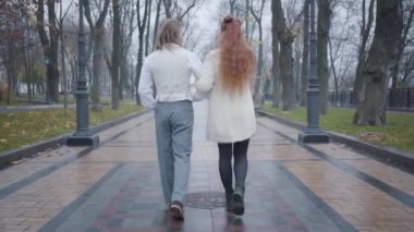 Güz parkında sokakta yürüyen beyaz bir çiftin arka görüntüsü. Mutlu erkek arkadaş ve kız arkadaşın dışarıda buluşması. Sıradışı erkek ve kadın retro giysiler içinde geziniyorlar..
