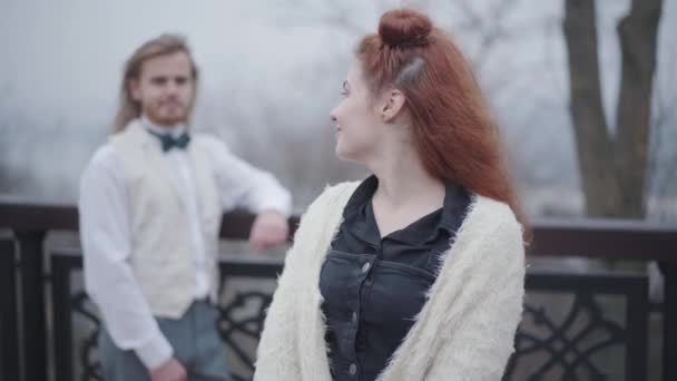 Belle femme caucasienne avec des petits pains doubles regardant en arrière à son petit ami portant chemise, gilet et noeud papillon, se tournant vers la caméra et souriant. Couple de style rétro datant dans le parc d'automne . — Video