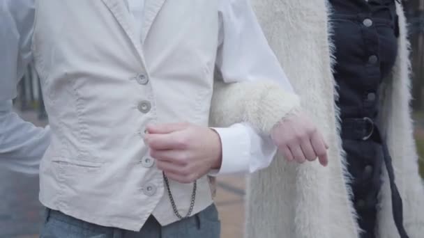 Close-up van mannelijke en vrouwelijke blanke handen. Vriend en vriendin die arm in arm lopen. Man in wit shirt en vest en vrouw in elegante kleding wandelen samen buiten. — Stockvideo