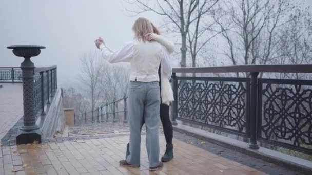 Молодая красивая кавказская пара танцует на мосту в осеннем парке. Красивый мужчина в стильной белой рубашке и жилете и рыжая женщина встречается на открытом воздухе. Счастливый парень и девушка отдыхают вместе . — стоковое видео