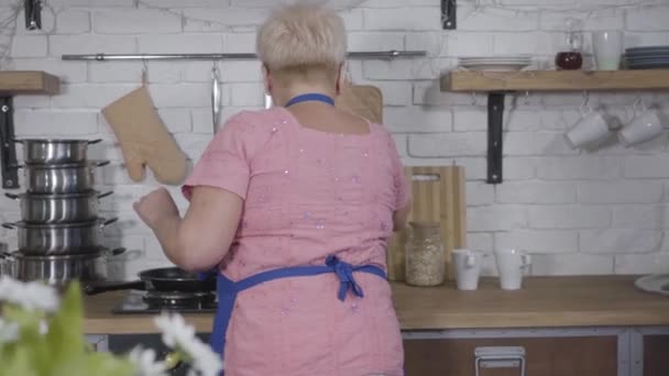 Achteraanzicht van oudere blonde blanke vrouw die boeket gele tulpen krijgt tijdens het koken in de keuken. Volwassen man geeft cadeau aan zijn schattige vrouw. Romantiek, eeuwige liefde. — Stockvideo