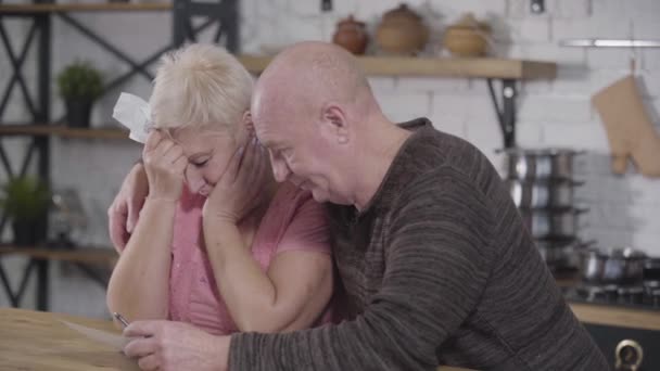 Vista lateral de pareja caucásica madura que resuelve sus ingresos y gastos. Hombre mayor calmando a su triste esposa y sonriendo. Financieros, jubilados, pagos . — Vídeos de Stock