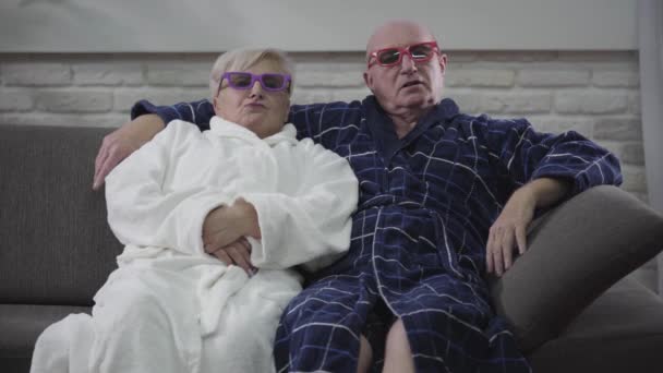 Весела кавказька старша пара сидить на дивані і рухається в залежності від фільму. Радісний чоловік і дружина відпочивають вдома після виходу на пенсію. Щастя, задоволення, веселощі, вічна любов. — стокове відео
