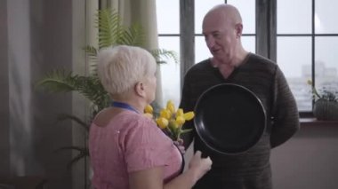 Kafkasyalı büyükannenin kocasını tavayla tehdit etmesi komik. Gülümseyen kel adam sarı lale buketiyle kendini savunuyor. Karısı suçlu eşini eğitiyor. Emekliler eğleniyor..