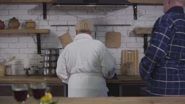 Grappige oude blanke man komt naar zijn vrouw en legt haar hand op haar kont. Verrassend positieve vrouw die opspringt. Grappig stel aan het knuffelen. Happy gepensioneerden hebben plezier binnen. — Stockvideo