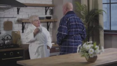 Olgun bir eşin önünde dans eden ve bornozunu açan komik, kel, beyaz adamın arkası. Elinde kahve fincanı olan kıdemli beyaz kadın küçümseyici bir şekilde ona bakıyor..