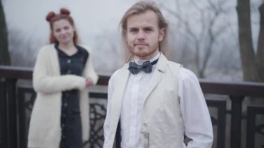 Retro elbiseli yakışıklı, beyaz bir adam arkasını dönüp güzel kız arkadaşına bakıyor, kameraya dönüp gülümsüyor. Sonbahar parkında flört eden eski moda çift..