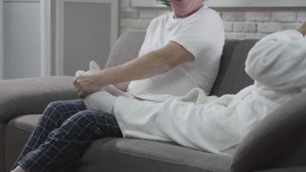 Nierozpoznawalny, dojrzały mężczyzna siedzący na kanapie i masujący stopy żonom. Mąż opiekuje się starszą żoną. Szczęśliwa para odpoczywa w domu. Wieczna miłość, troska, wspólnota. — Wideo stockowe