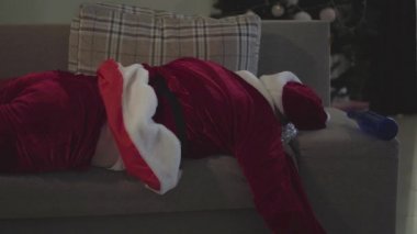Noel Baba kostümlü bitkin adam kanepede uyuyor. Evdeki kanepede yatan sarhoş adam. Kötü Noel Baba. Alkolizm, depresyon, negatiflik, yalnızlık..