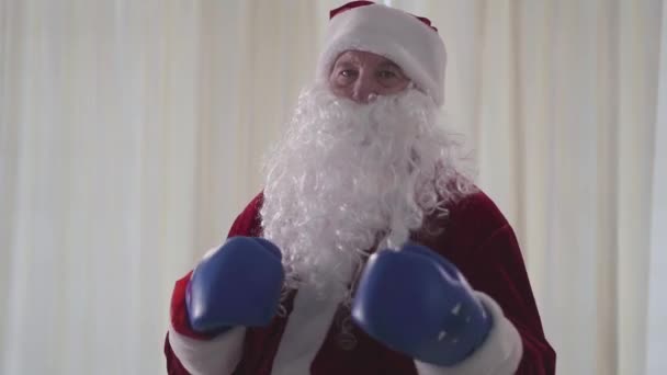 Retrato de Papai Noel barbudo de pé em luvas de boxe azuis e ameaçadoramente perfurando o ar. Personagem fictício maligno olhando para a câmera. Natal, feriado, mau Pai Natal . — Vídeo de Stock