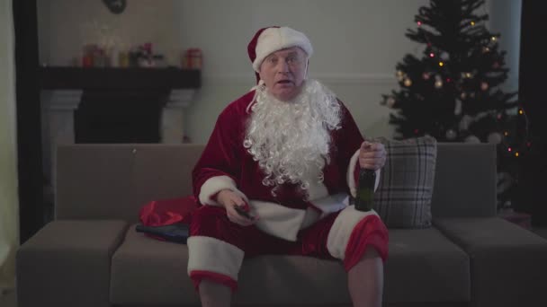 Vtipný muž běloch Santa Claus sedí na pohovce a dívá se na sportovní utkání na TV. Senior radostný fanoušek odpočinku doma po náročném pracovním dni. — Stock video