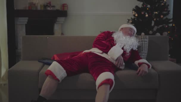 산타 클로스의 코스튬을 입은 늙은 백인 남자 옆에 빈 병이 놓여 있는 소파에서 자고 있었다. 다리벌리고 술취한 남자가 엉덩이를 긁고 있어. 안 좋은 산타. 알코올 중독, 비만증. — 비디오