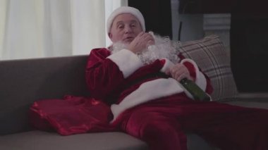 Noel Baba kostümlü, göğsünü kaşıyan ve uyuyan yaşlı beyaz adamın yakın çekimi. Yalnız ve olgun bir adam tatillerini bir şişe birayla geçiriyor. Kötü Noel Baba, yalnızlık, depresyon, alkolizm.