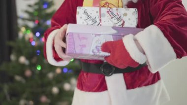 Noel Baba kostümü giymiş tanınmamış bir adam yılbaşı ağacının önünde hediye kutusunu geriyor. Hediye kutularını tutan adam. Mutlu bayramlar, gelenekler, Noel kavramı