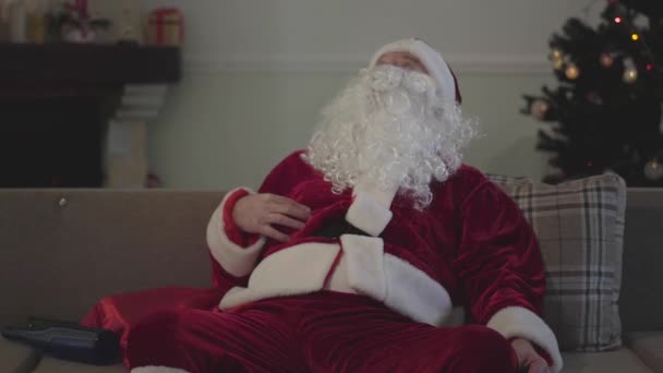 Vieil homme ivre mort en costume du Père Noël assis sur le canapé et buvant. Un Blanc solitaire qui passe ses vacances seul. Mauvais Père Noël, alcoolisme, négativisme . — Video