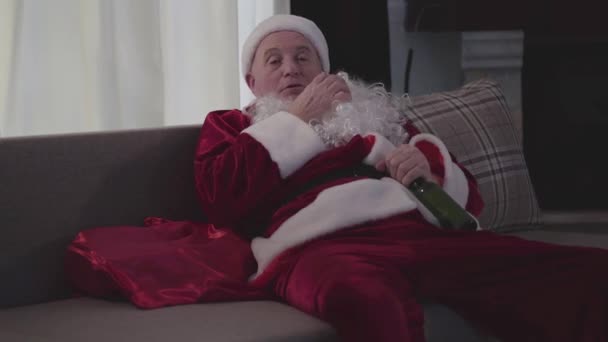 Close-up of old Caucasian man in Santa Claus costume scratching chest and falling asleep. Lonely mature guy spending holidays with bottle of beer alone. Bad santa, loneliness, depression, alcoholism. — Stock Video