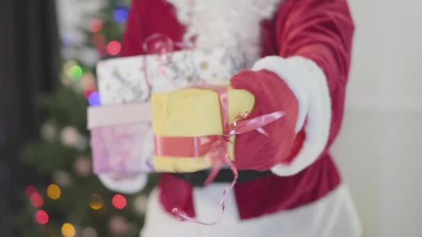 Noel Baba kostümü içinde tanınmayan bir adam yılbaşı ağacının önünde hediyeler veriyor. Hediye kutularını tutan adam. Mutlu bayramlar, gelenekler, Noel kavramı — Stok video