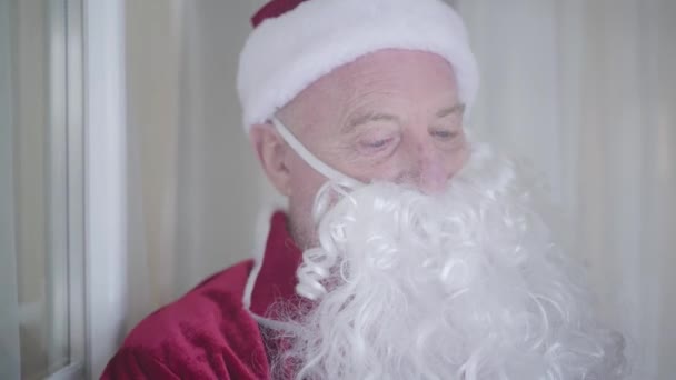 Retrato de un viejo feliz disfrazado de Santa Claus saludando con la mano y sosteniendo el presente. Concepto de felices fiestas, tradiciones, Navidad — Vídeos de Stock