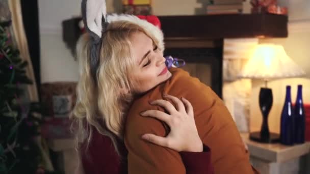 Närbild ansikte vacker blond vit kvinna med ögon slutna kramar oigenkännlig man. Glad flicka i kanin öron pannband med man eller pojkvän framför dekorerad julgran hemma. — Stockvideo