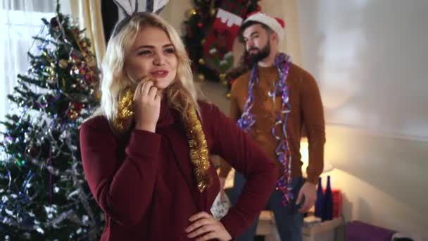 Porträtt av vacker vit flicka väntar otåligt som skäggig vit man står med presentförpackning i bakgrunden. Glada par tillbringa tid tillsammans på julafton hemma. — Stockvideo