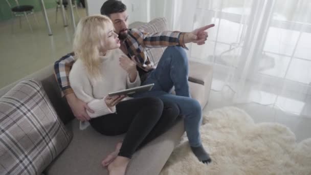 Vista dall'alto di giovane caucasico uomo e donna seduti sul divano e utilizzando tablet. Marito e moglie discutono di acquisti online per la loro casa. E-shopping, tecnologie wireless, Internet . — Video Stock