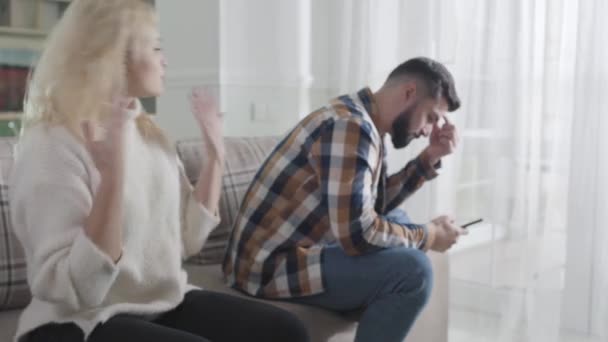Detailní záběr krásné mladé ženy křičící na muže sedícího s chytrým telefonem. Uražená žena je nespokojená s manželským přístupem. Vztah, manželství, komunikační problémy. — Stock video