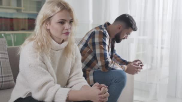 Een jong blank meisje dat wegkijkt als een man met een baard op de achtergrond. Man en vrouw hebben problemen in hun relatie. Uit elkaar gaan, misverstand, scheiding. — Stockvideo