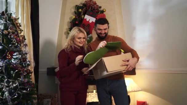 Vrolijk blond blank meisje neemt de decoratie uit de doos en hangt het aan haar man of vriendje. Joyful paar versieren huis en kerstboom op oudejaarsavond. — Stockvideo