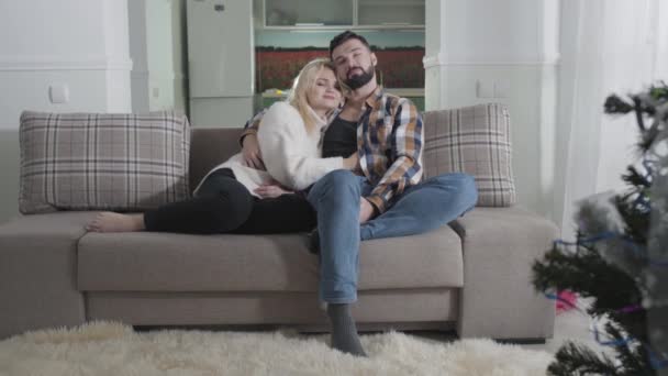 Retrato de marido y mujer caucásicos felices sentados en un sofá y abrazados. Pareja enamorada pasando los fines de semana juntos en casa. Ocio, descanso, unión . — Vídeo de stock