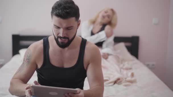 Blond attractive Caucasian woman sexually moving at the background as her husband or boyfriend playing video games at the foreground. Young games addicted guy ignoring intimate life. — Stock Video